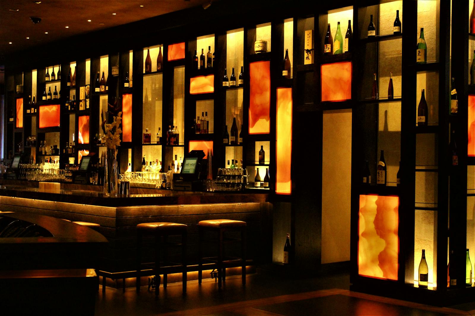 Beleuchtete Bar mit Weinflaschen und Barhockern